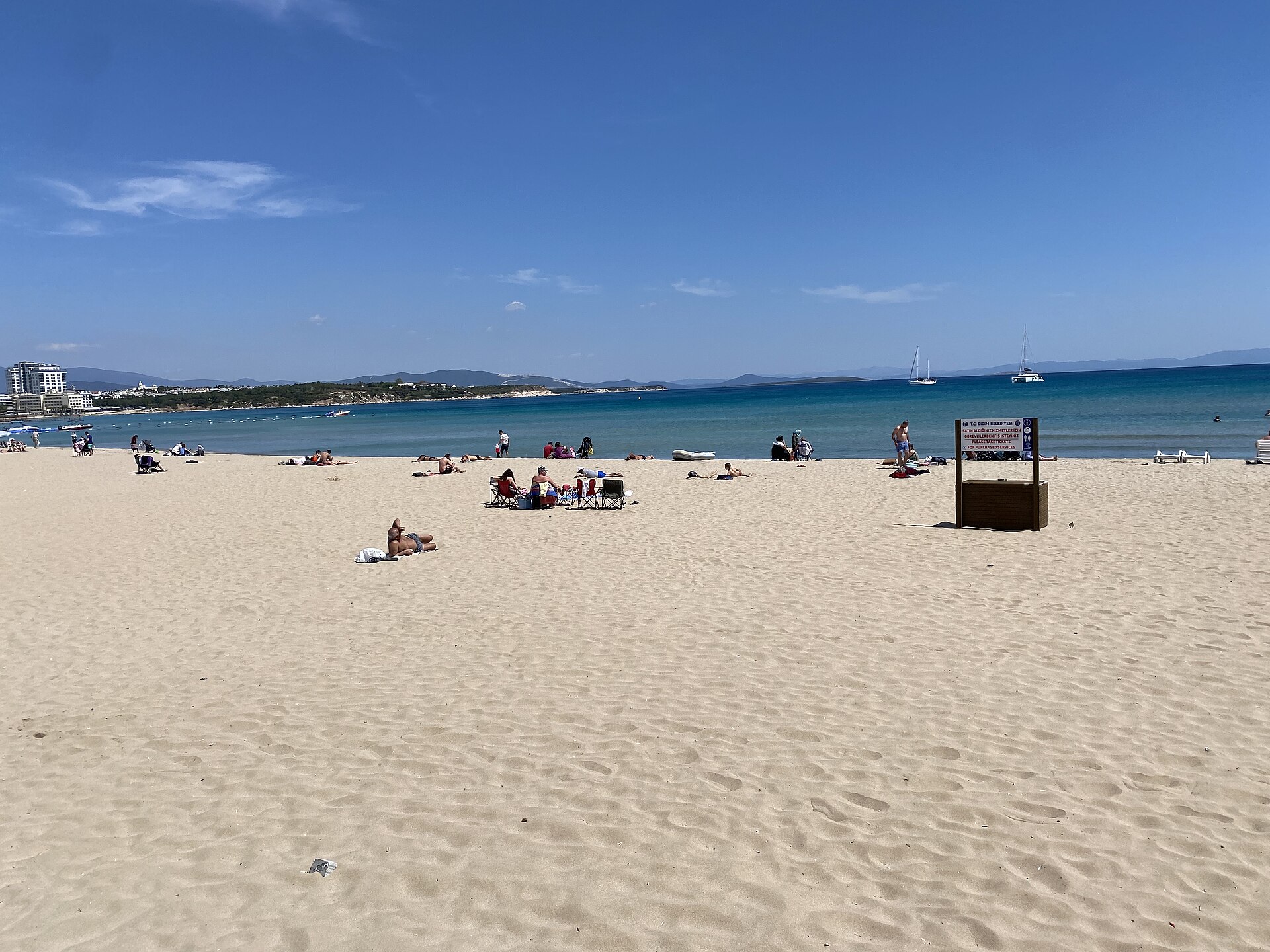 People relaxing beside the turquoise water and broad sandy shore of Altınkum Beach in Didim
